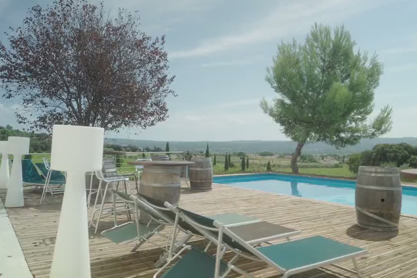Terrasse en bois avec transats et piscine, arbre et vallée en arrière-plan.