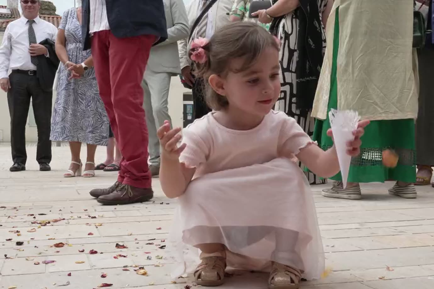 Une petite fille en robe rose ramasse des pétales au sol parmi les invités.